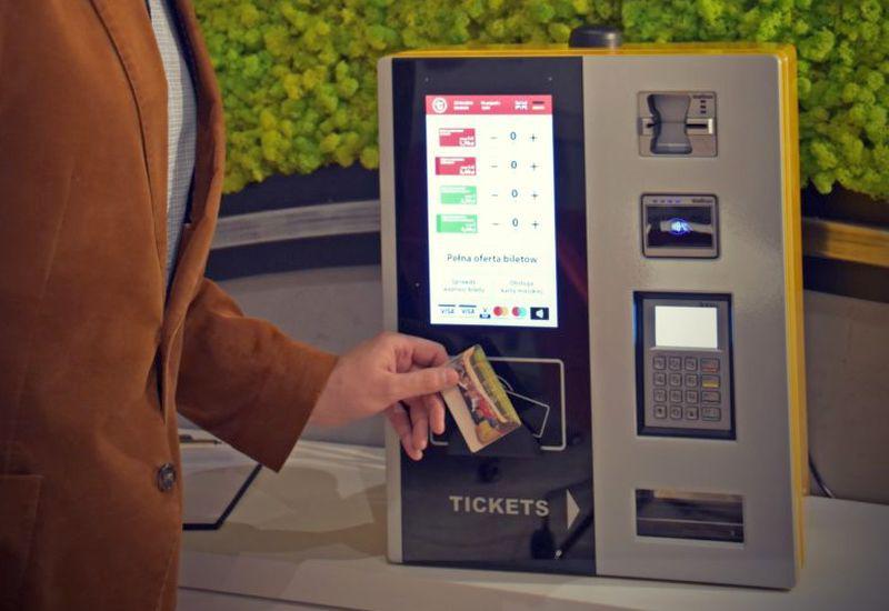Osoba korzystająca z automatu biletowego w celu zakupu biletów mobilnych. Na automacie wyświetla się napis „TICKETS”.