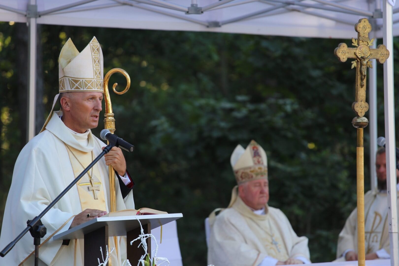 Biskup wygłasza kazanie na mszy na świeżym powietrzu. Przywódca religijny przemawia na podium.