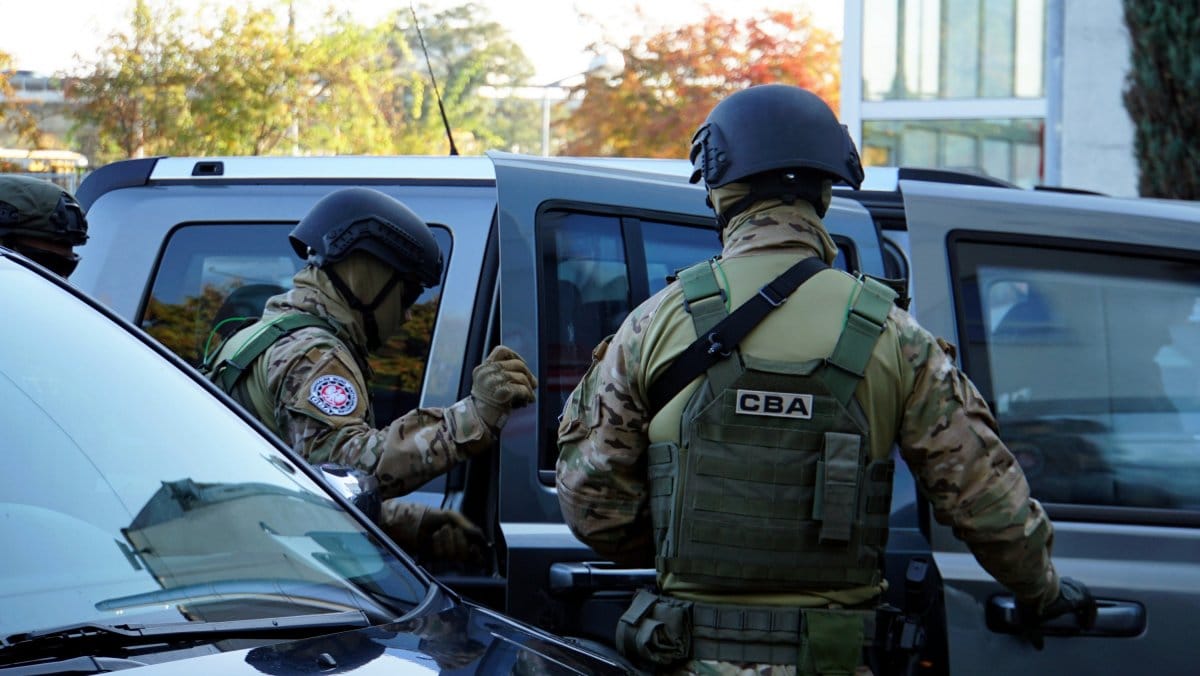 Funkcjonariusze Centralnego Biura Śledczego (CBA) w ubraniach taktycznych w pobliżu pojazdów.