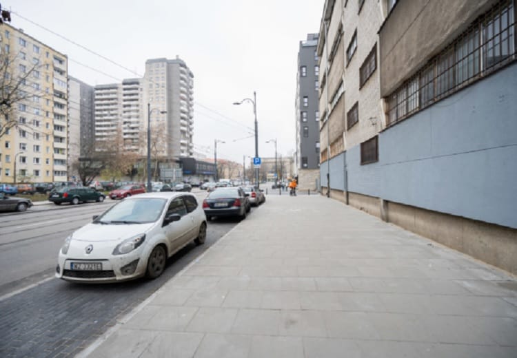 Scena uliczna miasta z zaparkowanymi samochodami i budynkami mieszkalnymi.