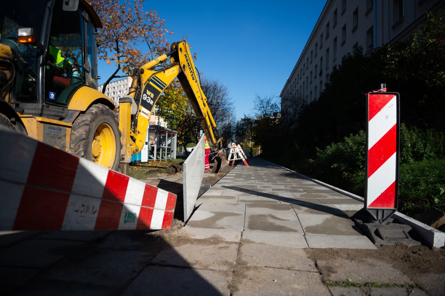 Pracownik budowlany używa koparki Komatsu WB93R do układania nowego chodnika.