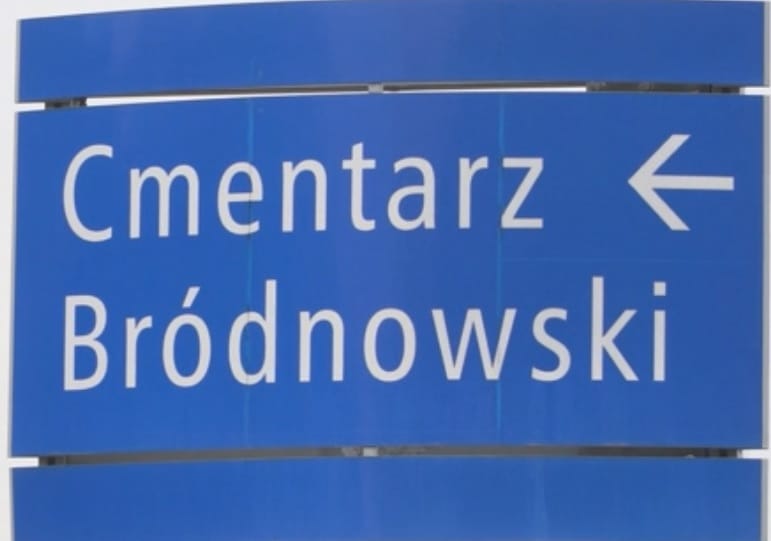 Niebieski znak wskazujący Cmentarz Bródnowski ze strzałką wskazującą skręt w lewo.