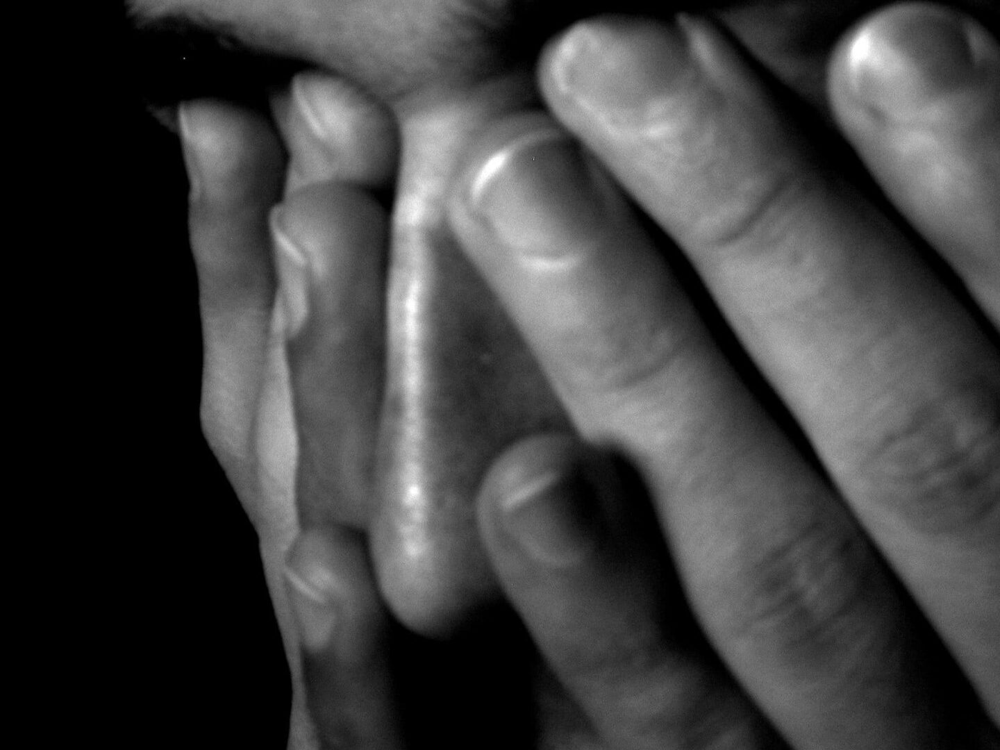 Zbliżenie twarzy człowieka zasłoniętej dłońmi, wyrażające smutek lub niepokój.