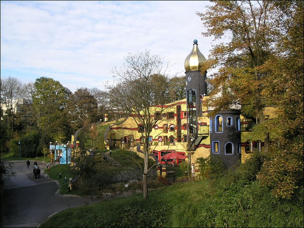 Fantazyjny, kolorowy budynek apartamentowy Hundertwassera, położony pośród bujnej zieleni.