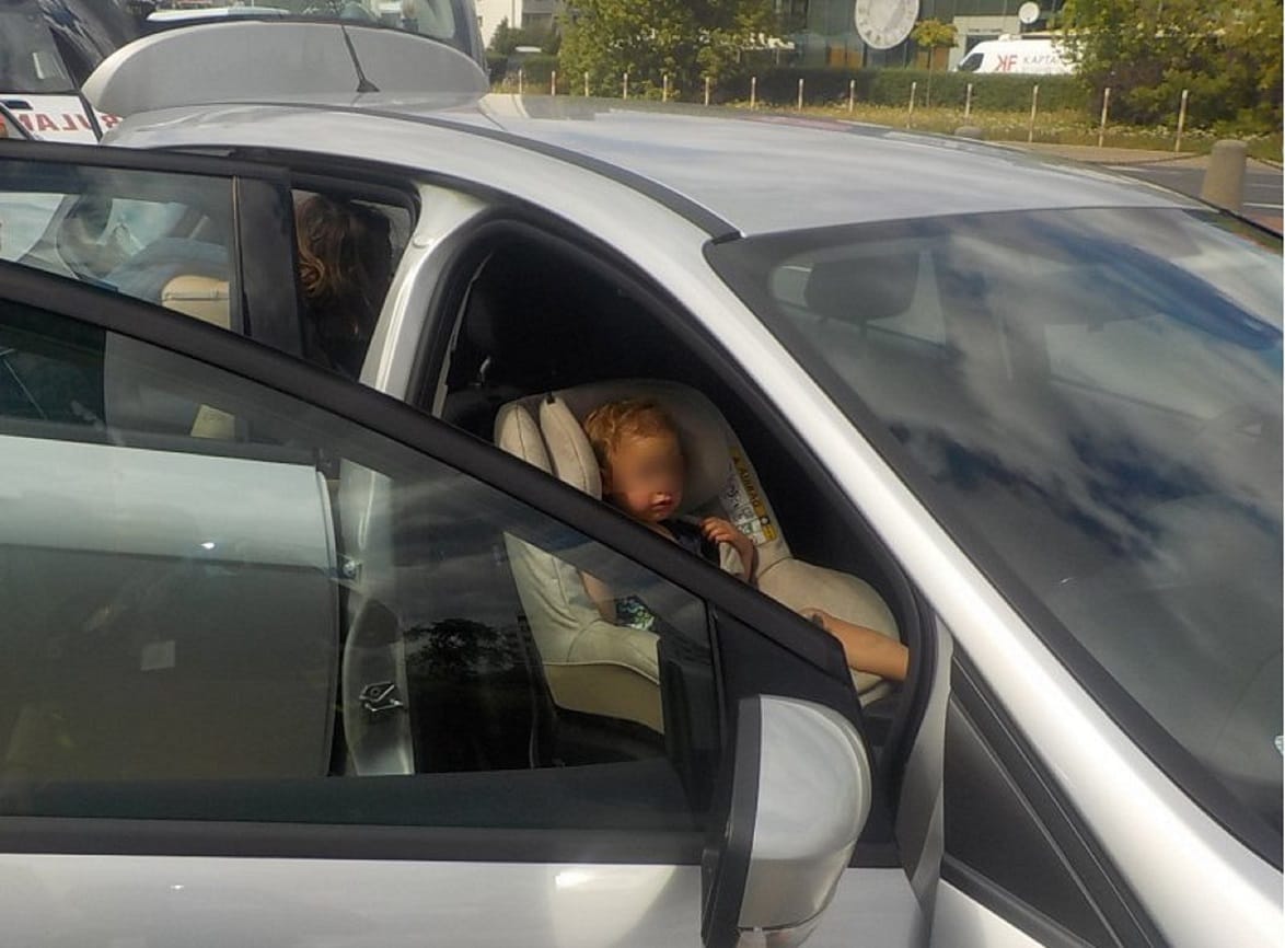 Maluch śpiący w foteliku samochodowym, mama na siedzeniu pasażera.