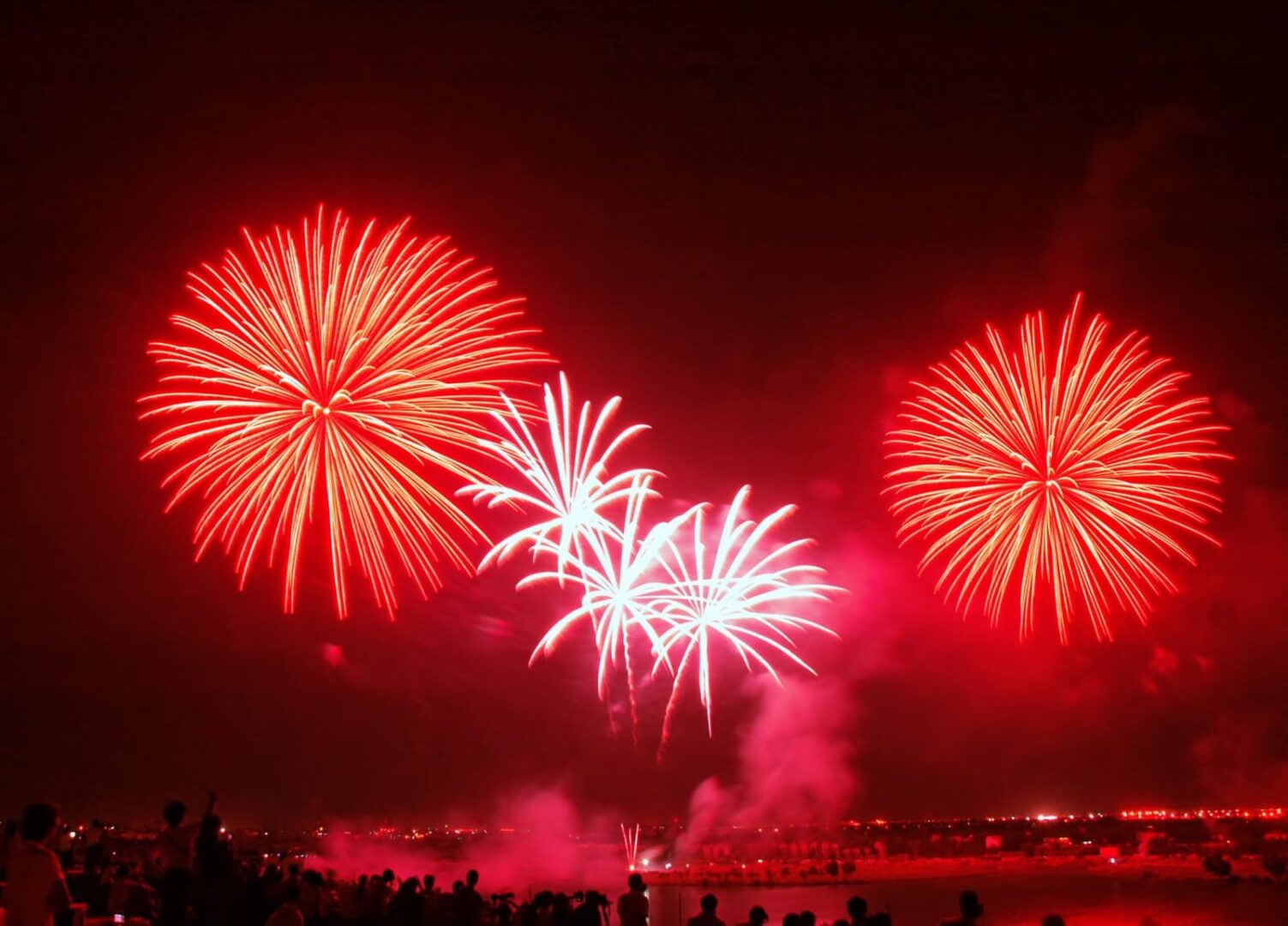 Na nocnym niebie wybuchają jaskrawoczerwone i białe fajerwerki.