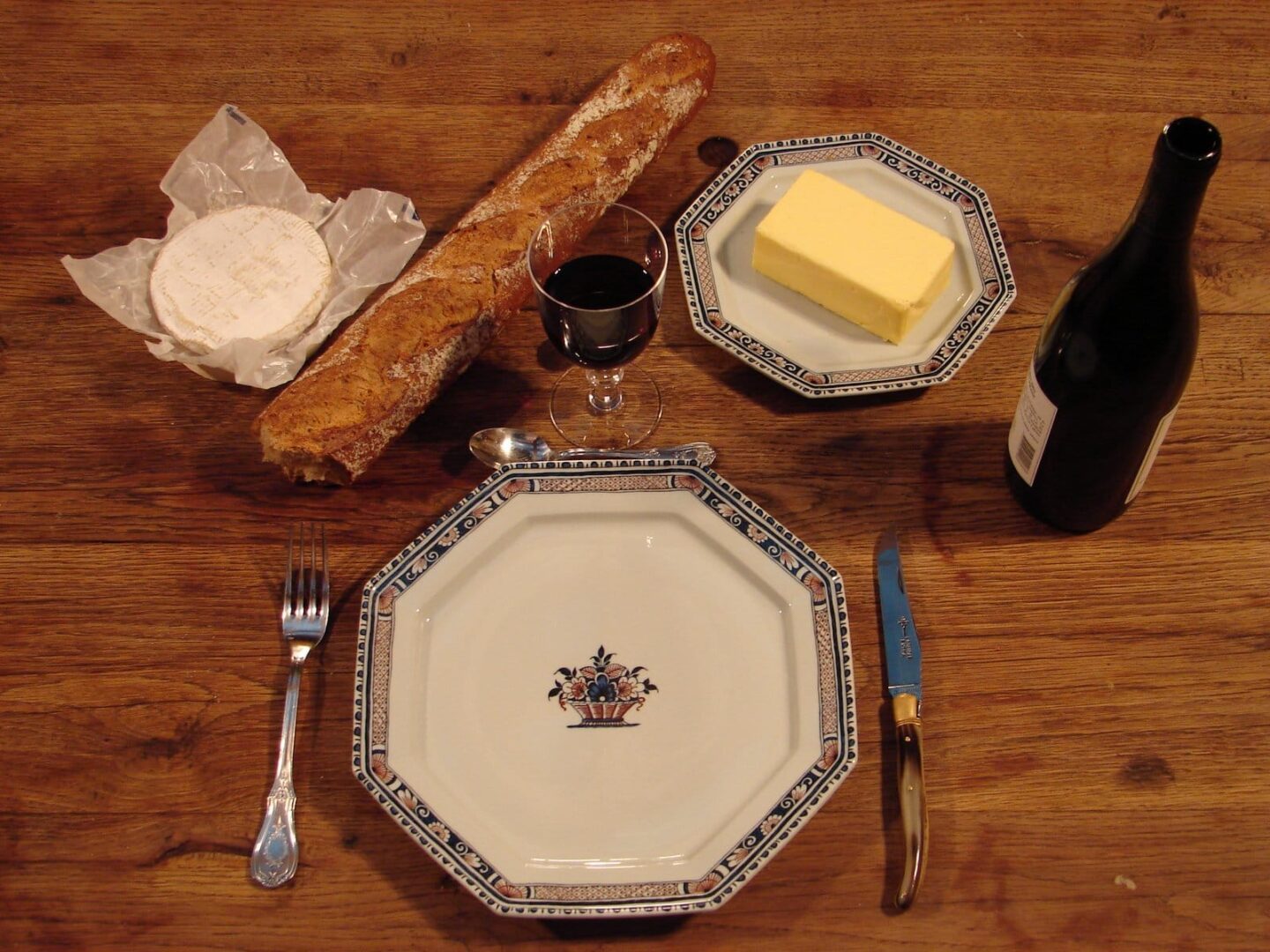 Rustykalne nakrycie stołu z bagietką, serem, masłem, winem i sztućcami.