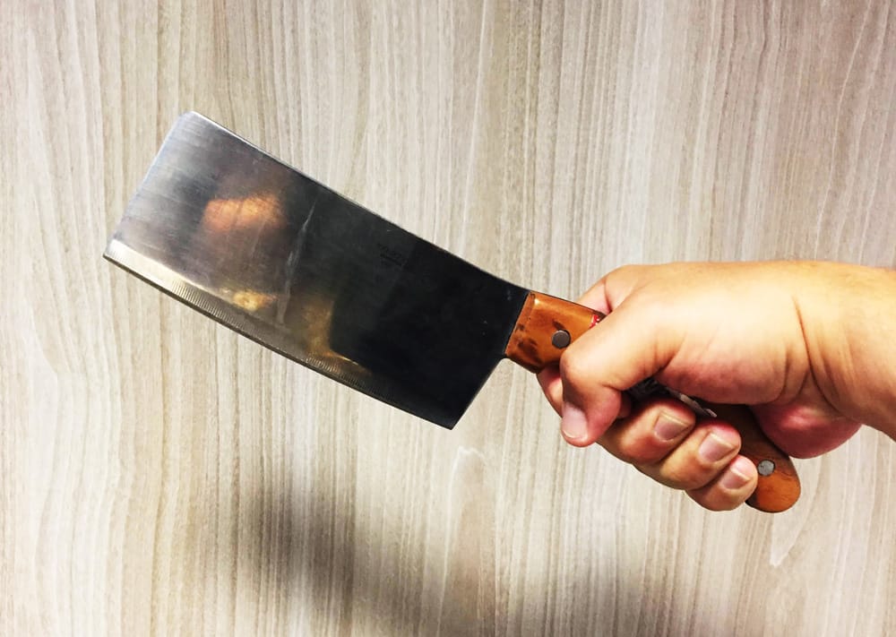 Zbliżenie dłoni trzymającej duży nóż rzeźniczy z drewnianą rękojeścią.