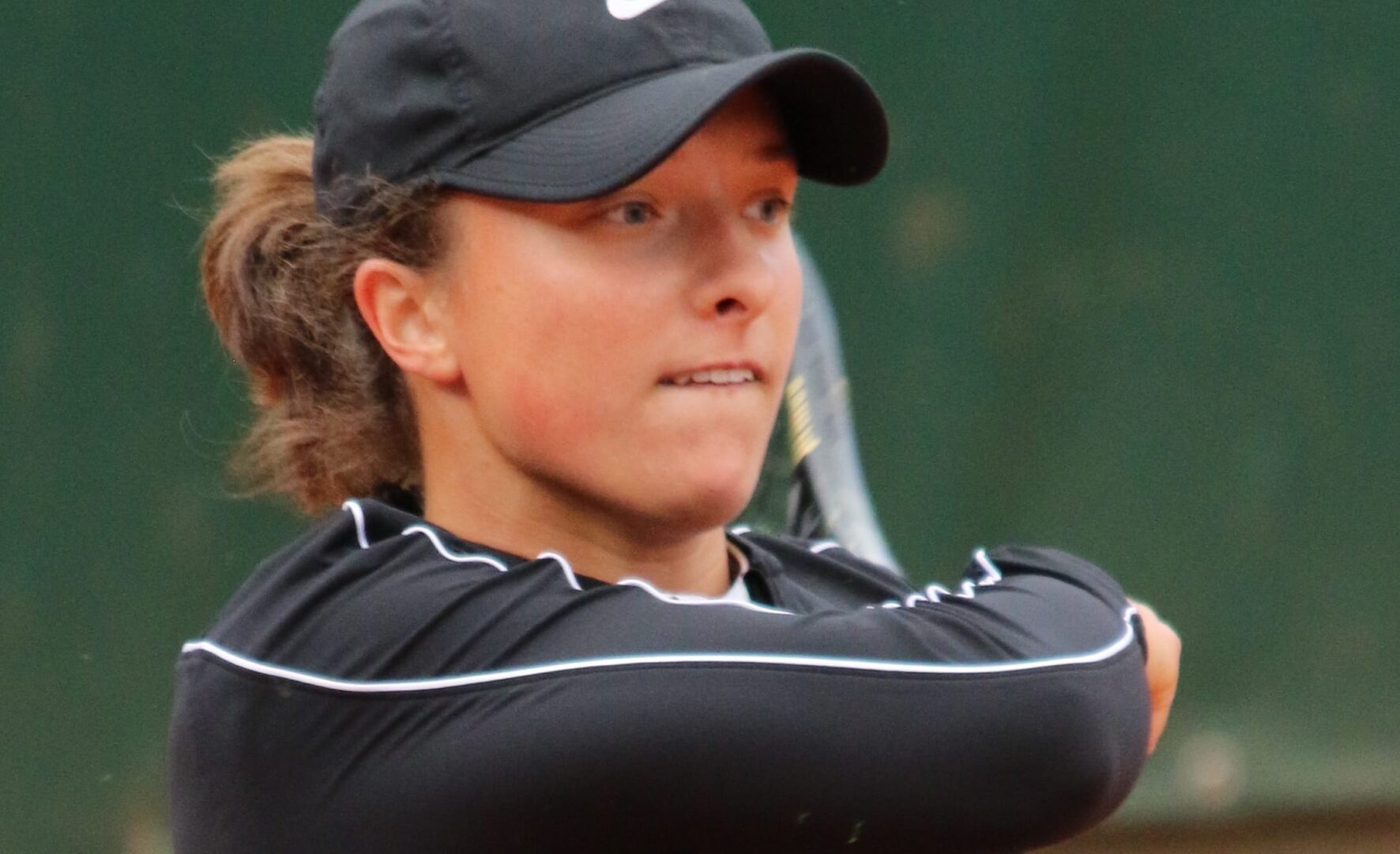 Młoda tenisistka w czarnym daszku, skupiona na grze.