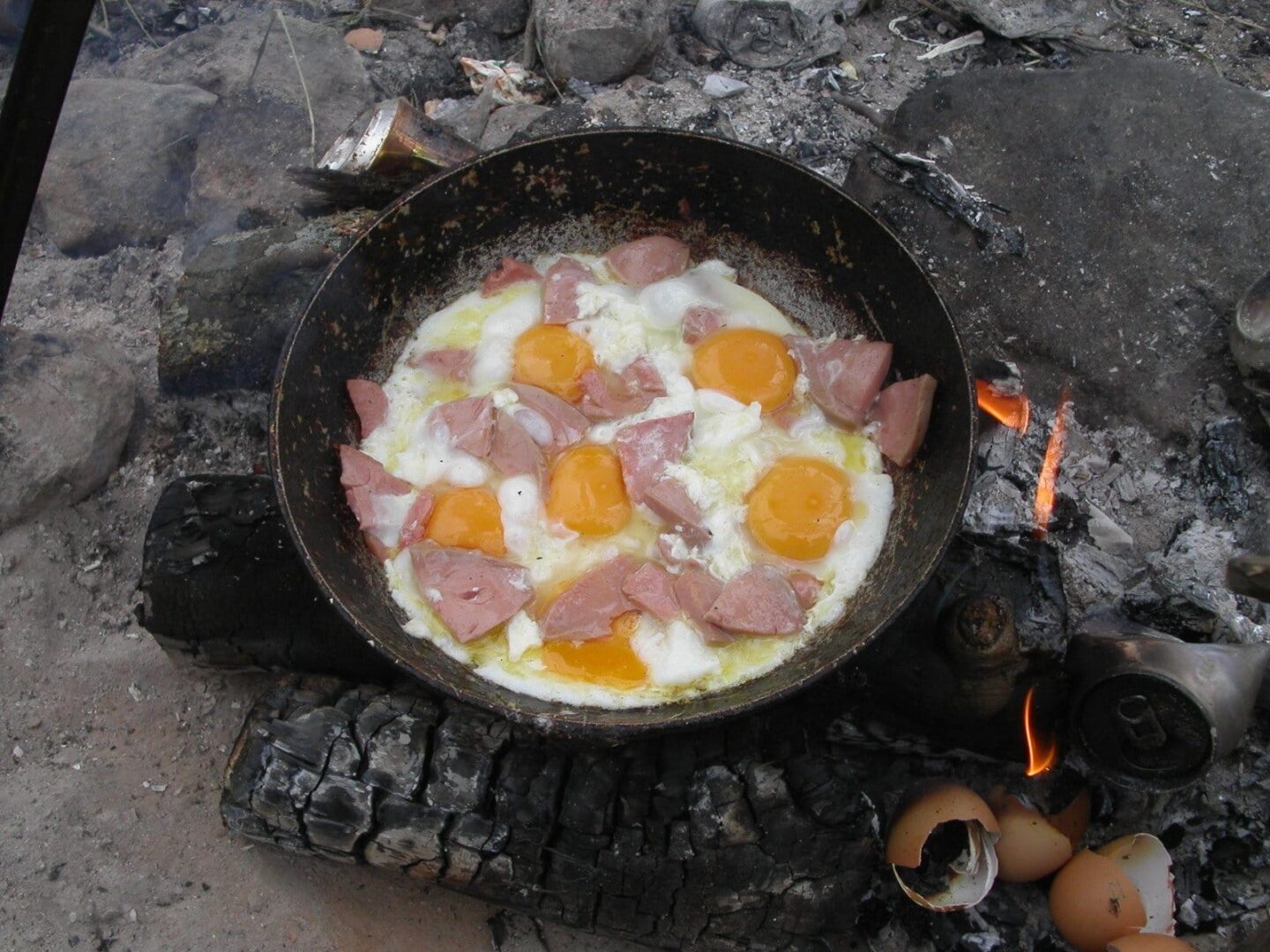 Śniadanie przy ognisku: jajka i mięso smażone na żeliwnej patelni nad otwartym ogniem.