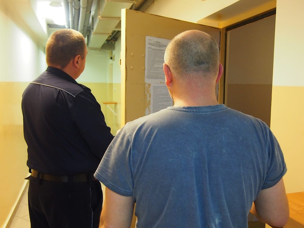 Dwóch mężczyzn, jeden w ciemnym mundurze, stoi na korytarzu. Zakaz prowadzenia pojazdów, jazda po pijanemu i wyrok sądowy są sugerowane.