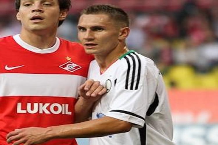 Dwóch piłkarzy, jeden w czerwono-białej koszulce Lukoil, drugi w biało-czarnej koszulce, wchodzą w interakcję na boisku.