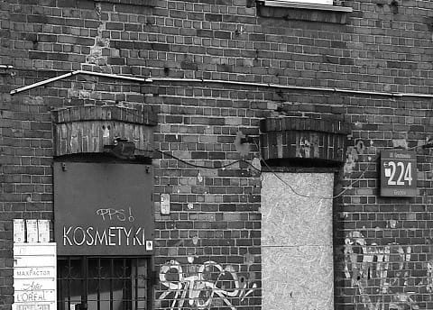 Budynek z cegły pokryty graffiti, z napisem „Kosmetyki” i numerem 224