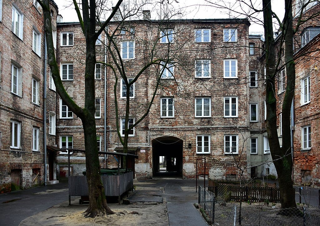 Ceglany dziedziniec z drzewami i budynkiem mieszkalnym. Stara architektura.