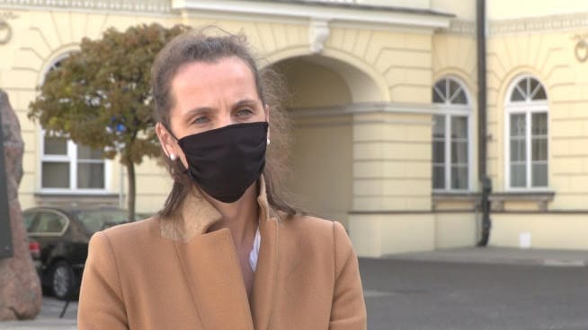 Kobieta w brązowym płaszczu i czarnej masce na twarzy