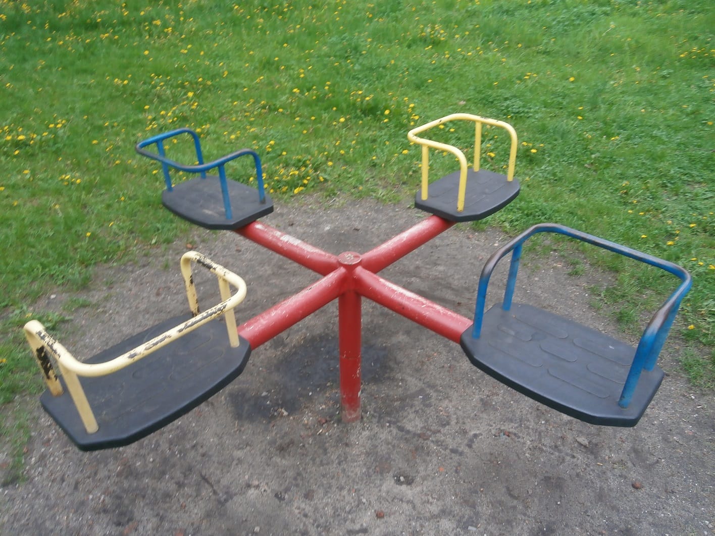 Karuzela na placu zabaw z czterema kolorowymi siedziskami.