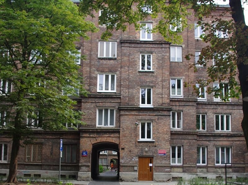 Ceglany budynek mieszkalny z łukowatym wejściem, prezentujący klasyczną architekturę.