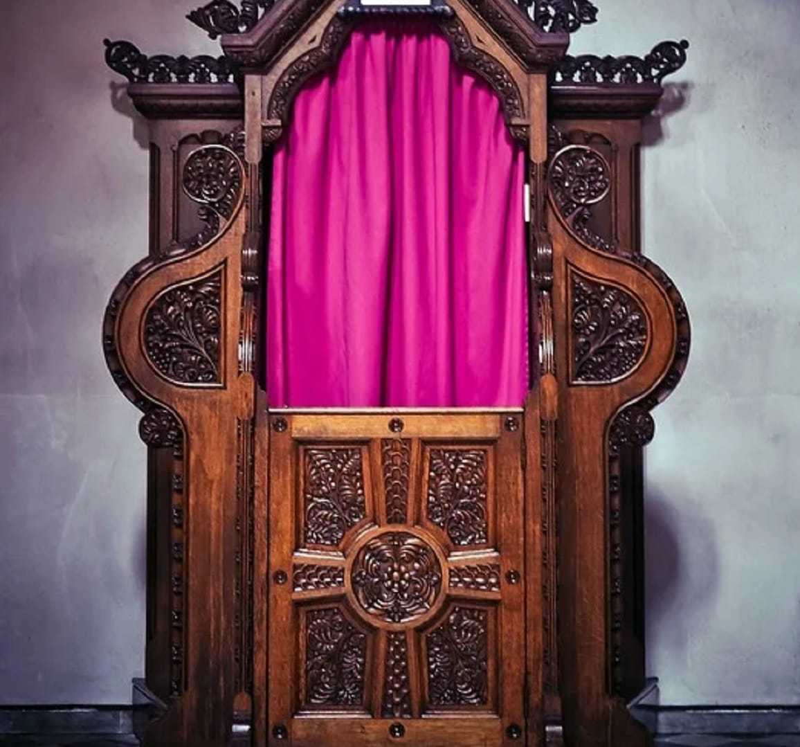 Ozdobny drewniany konfesjonał z różową zasłoną, oferujący miejsce do modlitwy i spowiedzi, nawet w czasie kwarantanny.