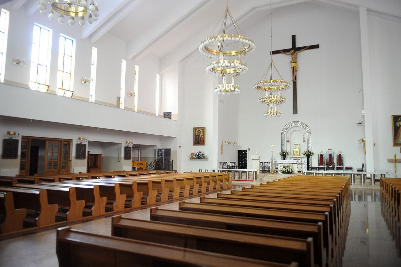 Puste ławki w nowoczesnym wnętrzu kościoła z żyrandolami i krucyfiksem.