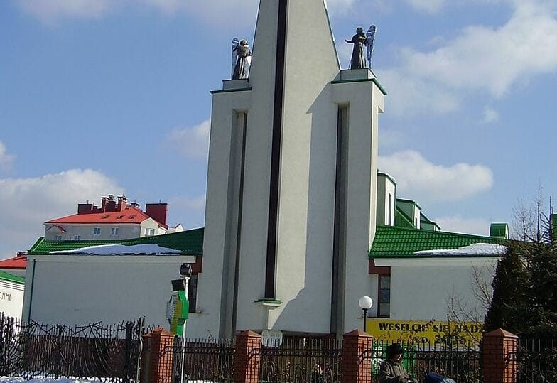 Nowoczesna fasada kościoła z figurami aniołów, zielonym dachem i napisem "Wesele".