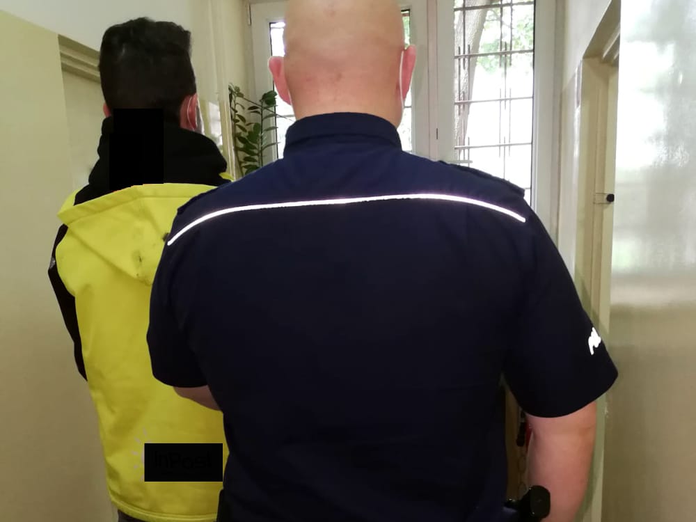 Policjant eskortujący podejrzanego korytarzem.