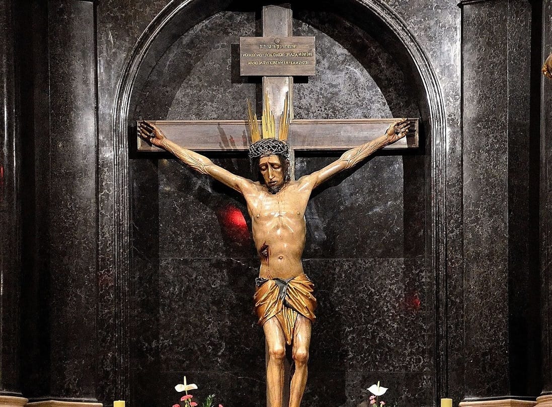 Statua ukrzyżowania w ciemnej marmurowej wnęce.