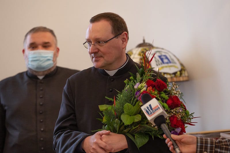 Ksiądz otrzymuje kwiaty i gratulacje, w tle inny ksiądz