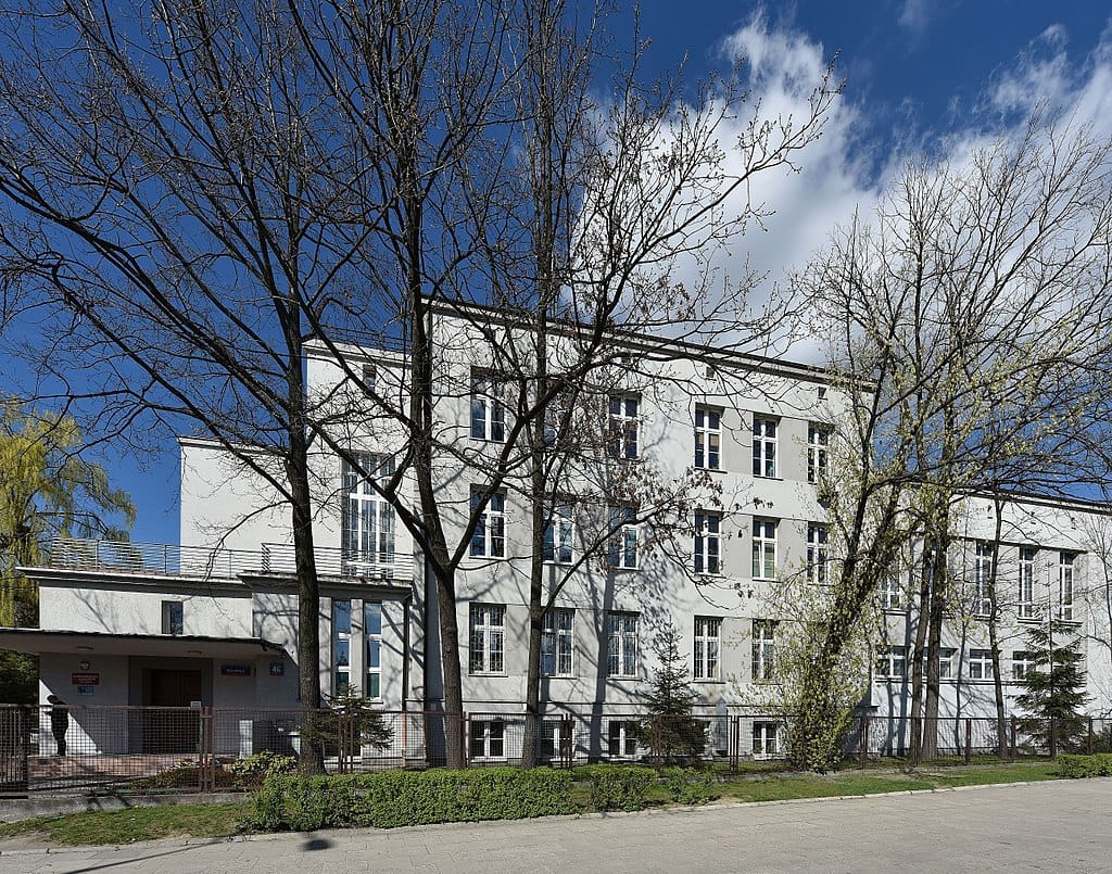 Nowoczesny biały budynek z wieloma oknami, otoczony nagimi drzewami.