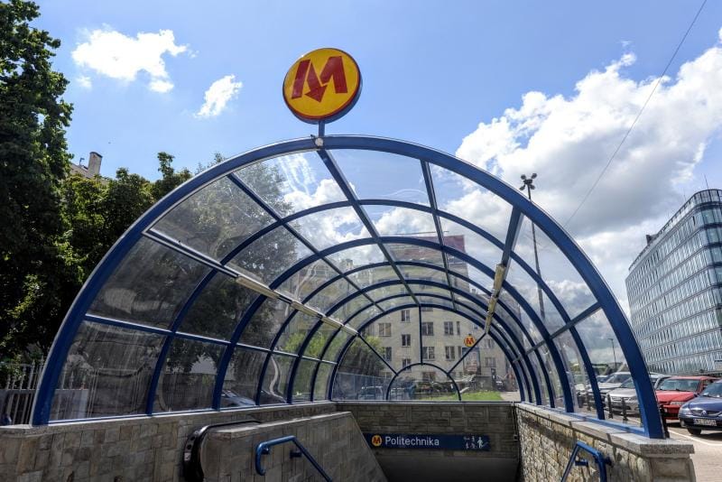 Wejście na stację metra Politechnika w Warszawie, z zakrzywionym szklanym i metalowym daszkiem.
