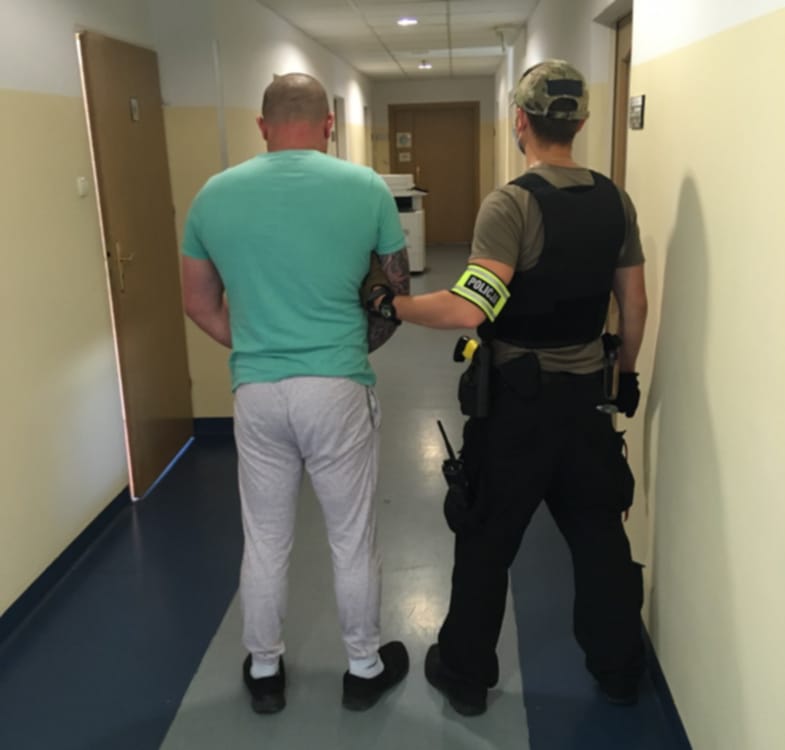 Policjant eskortujący podejrzanego korytarzem szpitalnym.