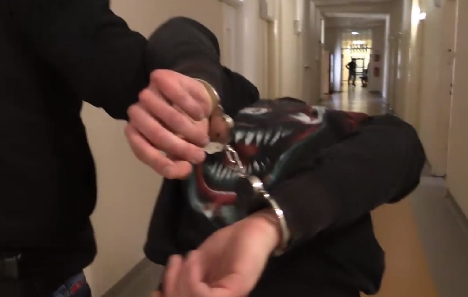 Policjant zakładający podejrzanemu kajdanki na korytarzu