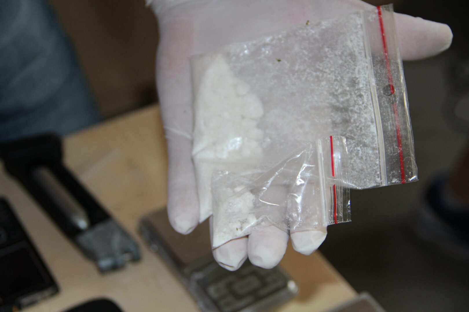 Zbliżenie dłoni w rękawiczce trzymającej woreczek z białym proszkiem, prawdopodobnie zabezpieczony dowód.