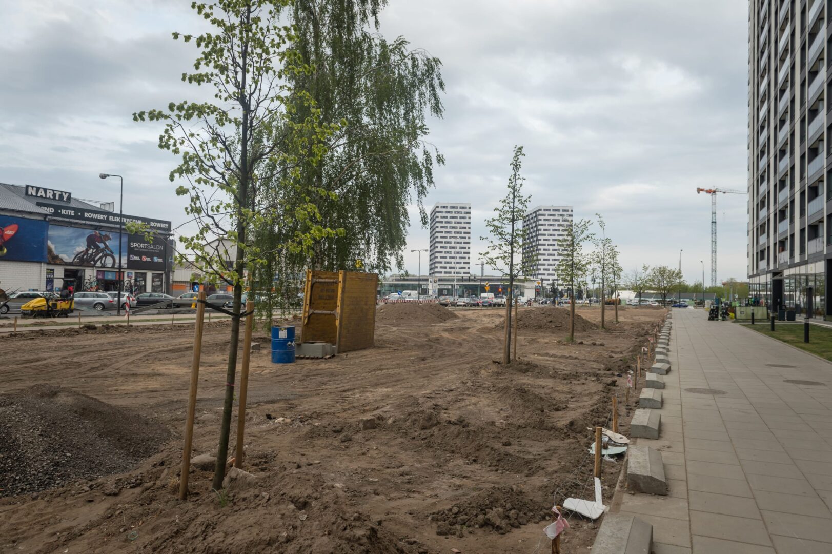 Miejski plac budowy z nowymi budynkami i sadzonymi młodymi drzewami.