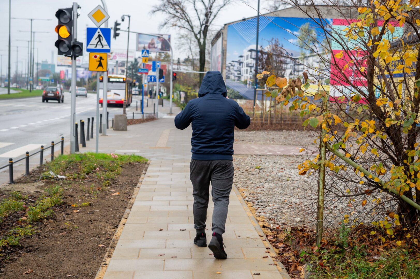 Mężczyzna idący chodnikiem w pobliżu ruchliwej ulicy, jesienne liście