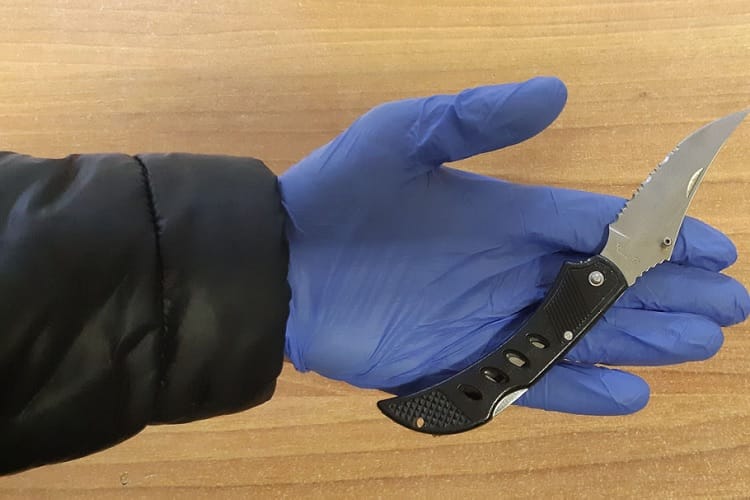 Zbliżenie dłoni w rękawiczce trzymającej czarny składany nóż.