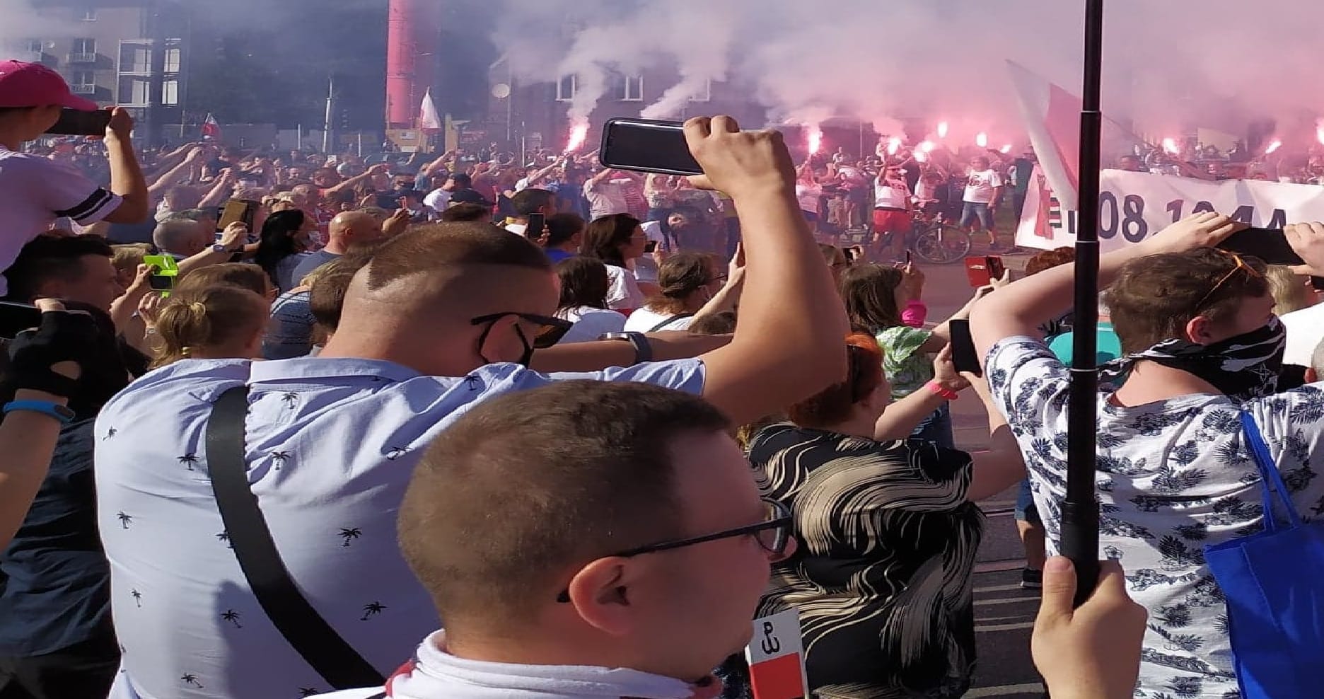 Tłum ludzi na marszu z okazji Dnia Niepodległości Polski, trzymających telefony i flagi.