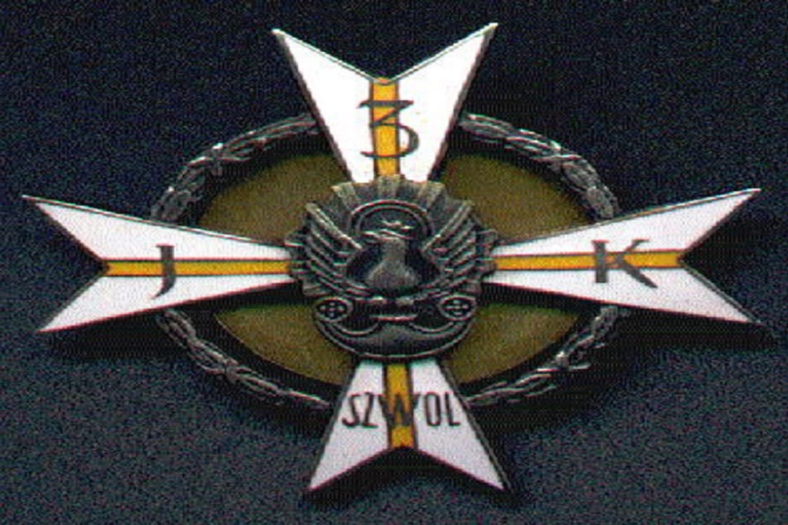Srebrna odznaka z krzyżem Szwola ze znaczeniami J i K, orłem pośrodku i wieńcem laurowym.