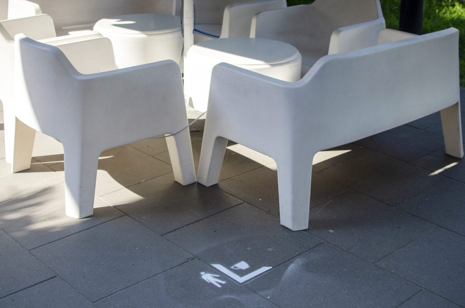 Białe plastikowe krzesła i stoły na tarasie z symbolem dystansu społecznego namalowanym na ziemi.