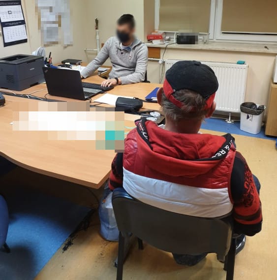 Dwóch mężczyzn na posterunku policji, jeden przy biurku, jeden siedzący. Przesłuchanie przez policję.