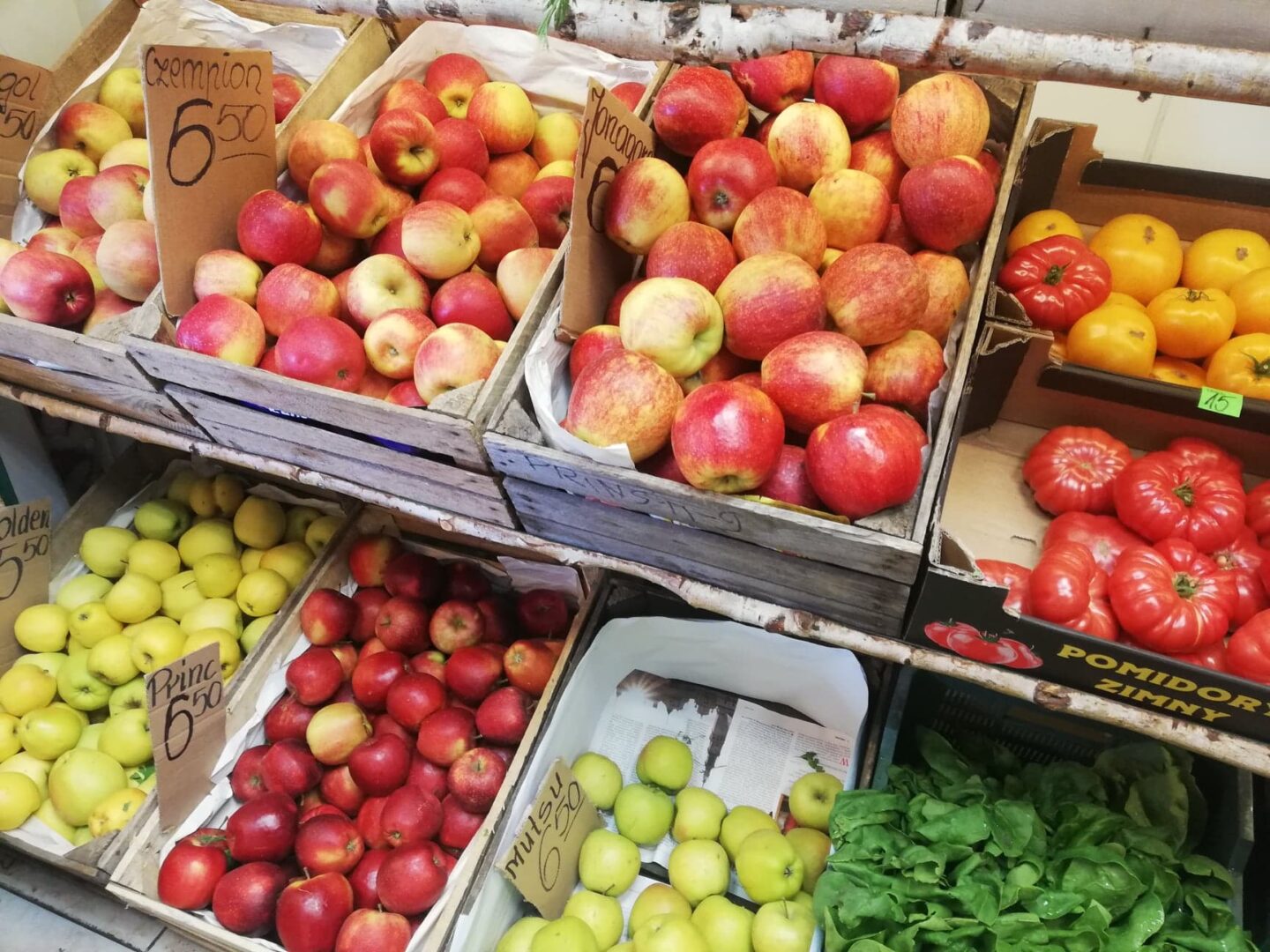 Świeże jabłka i pomidory w drewnianych skrzynkach na targu rolniczym. Ceny są widoczne.