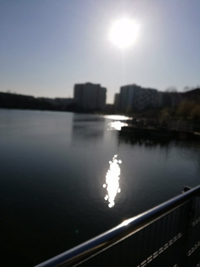 Słońce odbija się w spokojnej wodzie jeziora w pobliżu miejskich budynków.