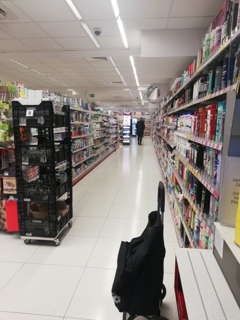 Alejka w supermarkecie z półkami wypełnionymi produktami kosmetycznymi i do pielęgnacji ciała. Wózek sklepowy.