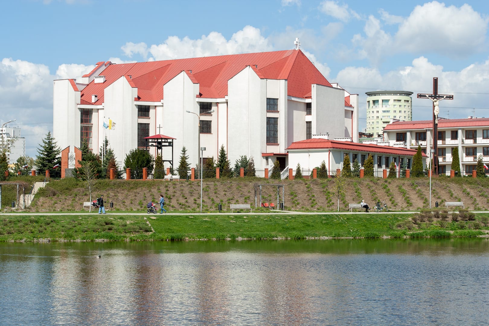 Nowoczesny kościół z czerwonym dachem, spokojnym jeziorem i ludźmi spacerującymi obok