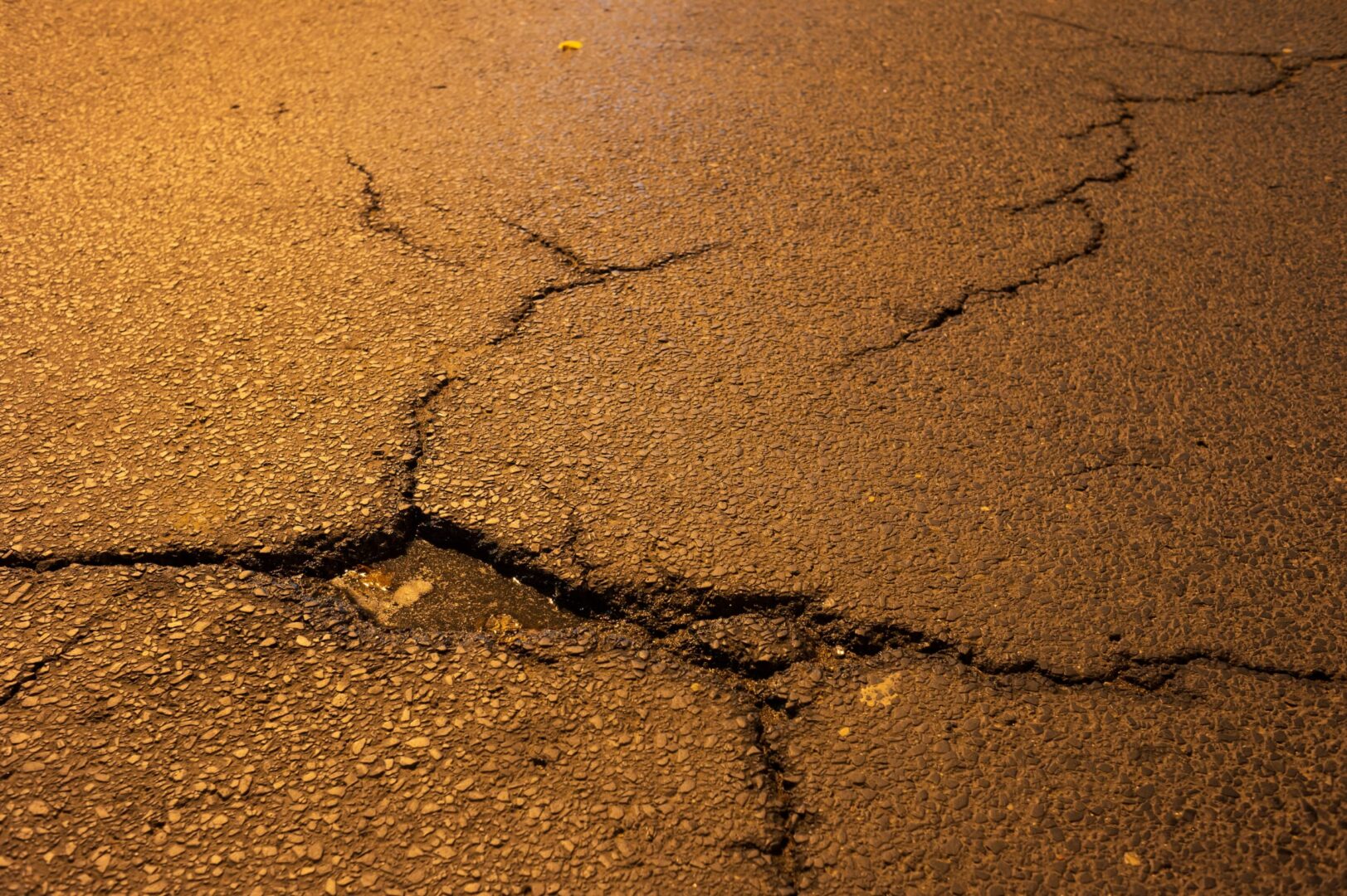 Popękana asfaltowa nawierzchnia drogi z kałużą. Uszkodzenie drogi, konieczna naprawa nawierzchni.