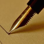 Zbliżenie złotej stalówki pióra wiecznego na papierze, piszącej.