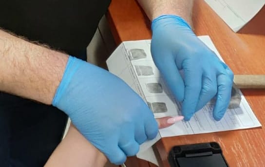 Zbliżenie dłoni w rękawiczkach pobierających odciski palców, widoczny tusz i papier.