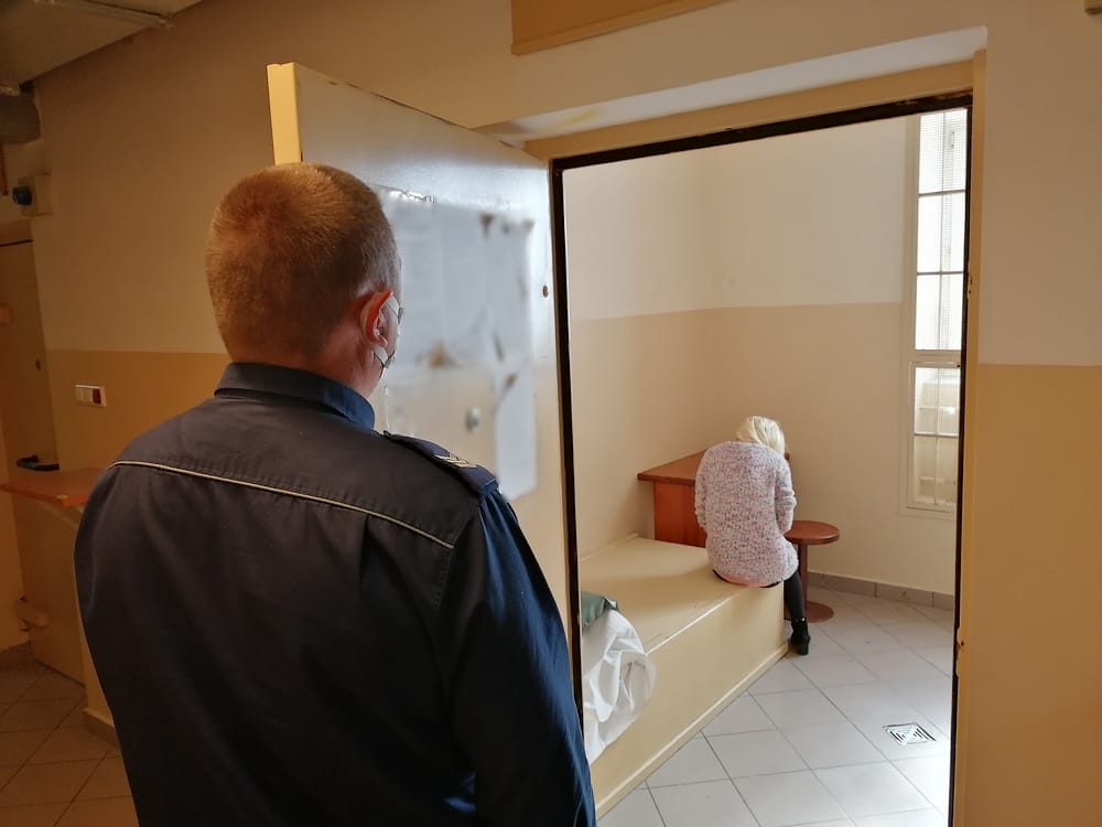 Policjant obserwuje zatrzymaną kobietę w celi więziennej.