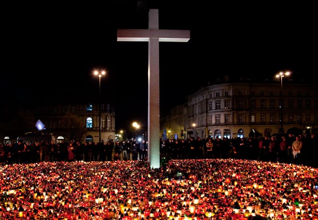 Duży biały krzyż nocą otoczony setkami zapalonych świec, czuwanie.