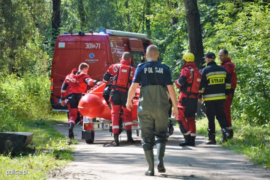 Ratownicy medyczni przy czerwonym wozie strażackim, przewożącym sprzęt ratowniczy.