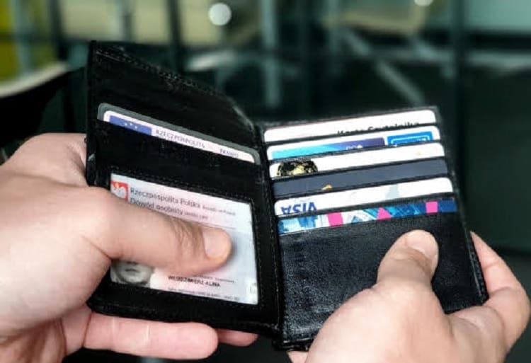 Dłonie trzymające czarny skórzany portfel zawierający karty kredytowe i polski dowód osobisty.